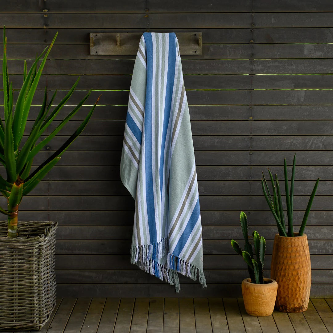 A Protea Pinstripe throw  hanging neatly on a wooden coat rack. Its hand-knotted fringes and versatile design make it perfect for both indoor and outdoor use. #GuestSatisfaction #UpgradeYourLodge #LodgeLife