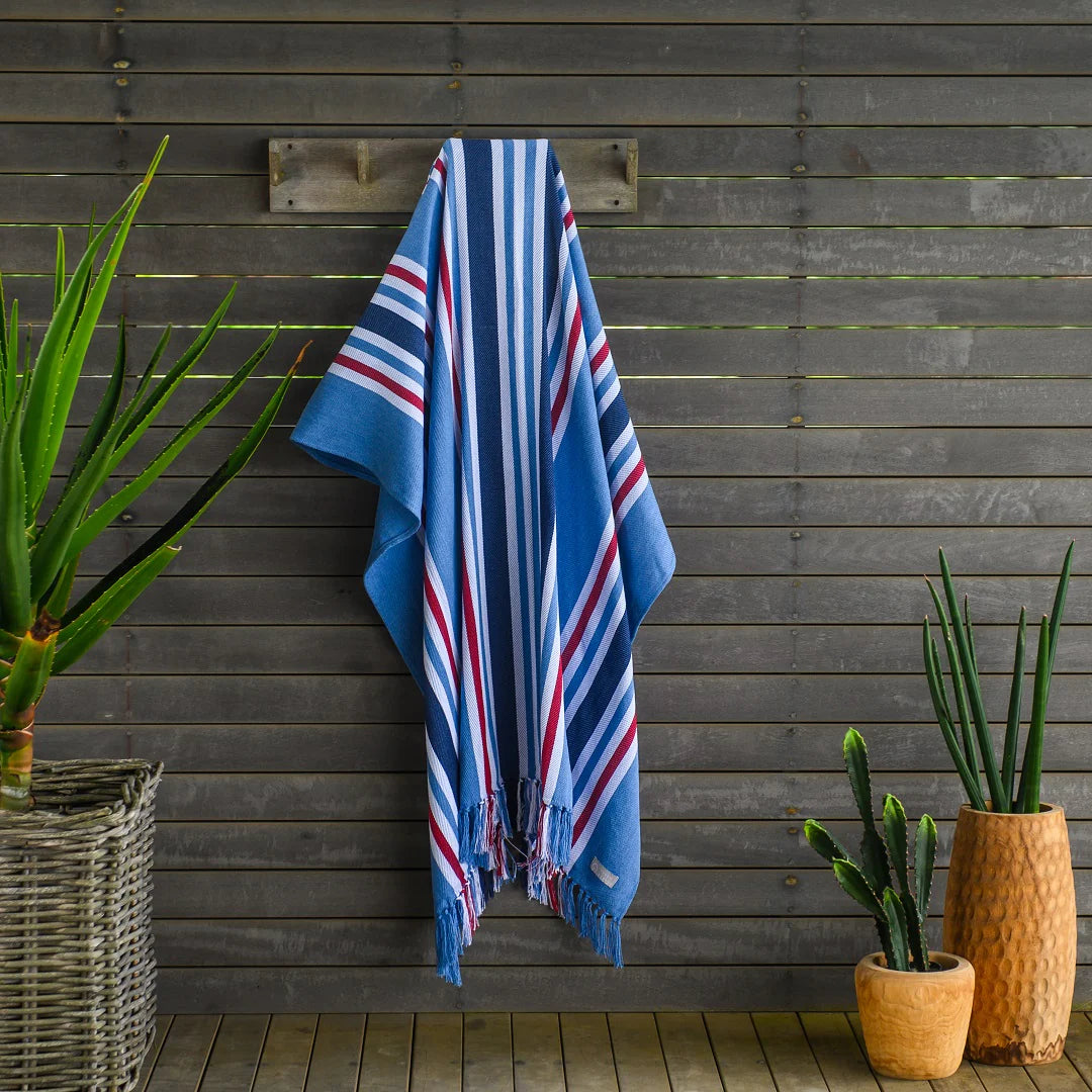 A Protea Pinstripe throw  hanging neatly on a wooden coat rack. Its hand-knotted fringes and versatile design make it perfect for both indoor and outdoor use. #GuestSatisfaction #UpgradeYourLodge #LodgeLife