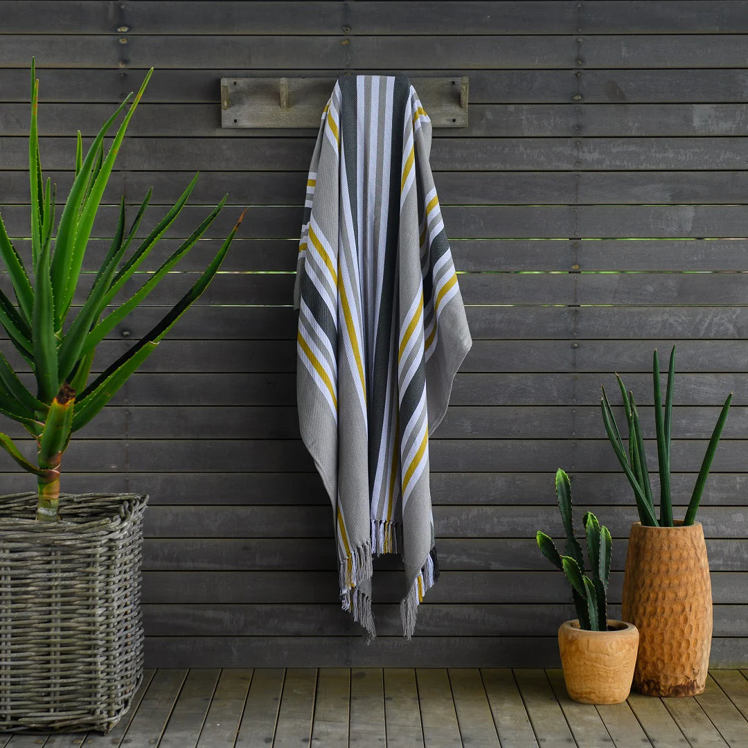 A Protea Pinstripe throw  hanging neatly on a wooden coat rack. Its hand-knotted fringes and versatile design make it perfect for both indoor and outdoor use. #GuestSatisfaction #UpgradeYourLodge #LodgeLife