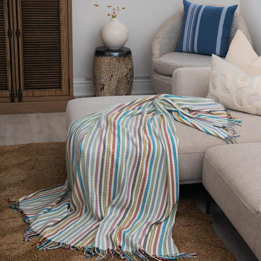 A Lyric Candy Stripe throw, featuring vibrant stripes in a playful and colorful pattern, draped over a sofa. Perfect for adding charm and personality to any lodge or guesthouse room. #LodgeLuxury #GuestExperience #PremiumBlankets #HospitalityExcellence #ProudlySouthAfrican